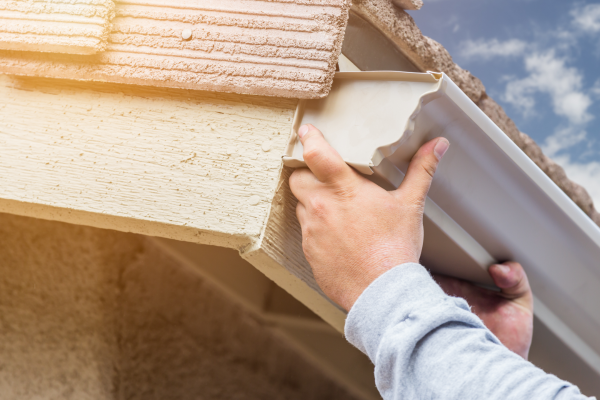 Image of a hand installing a gutter to the side of a house, Common Gutter Materials & Which is Best For Your Home
