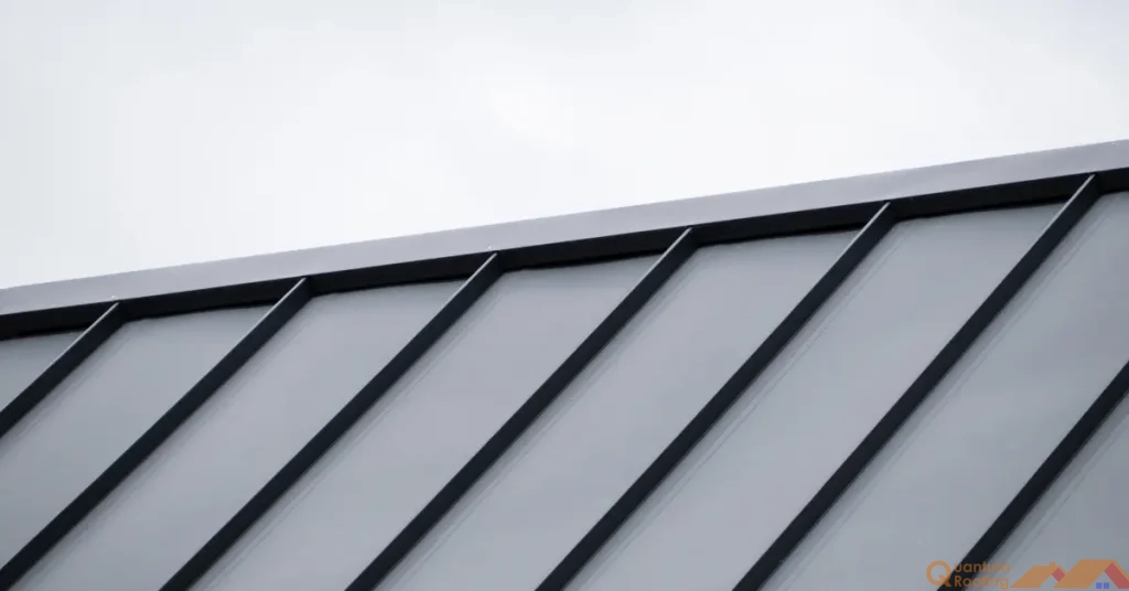 Standing seam metal roof ridge with a grey sky behind.