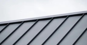 Standing seam metal roof ridge with a grey sky behind.
