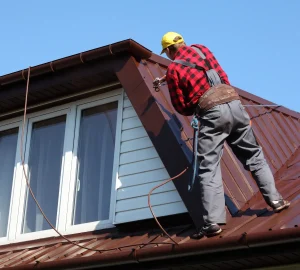 Roofing contractor installing a standing seam metal roof while wearing a safety harness