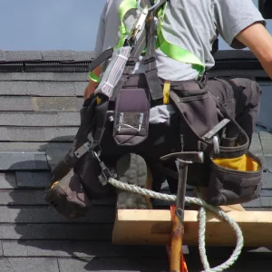 Roofer tethered to the shingle roof with a safety harness, working on a roof repair.