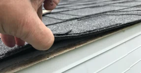 Inspector checking under the shingles during a roof inspection